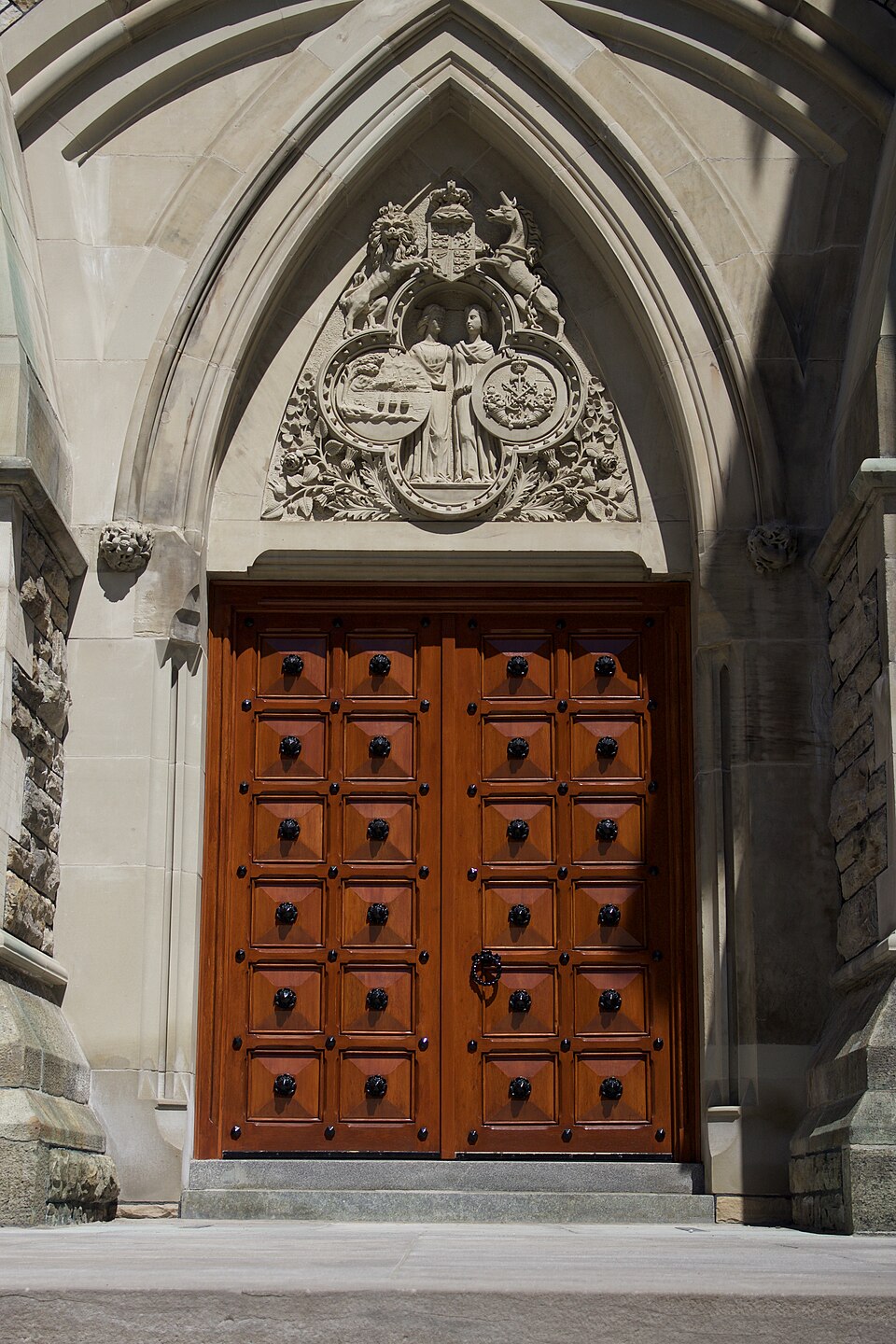 The ceremonial entrance of East Block, Parliament Hill: a pointed Gothic arch in pale sandstone over heavy studded timber doors, with a carved tympanum of the royal arms above.