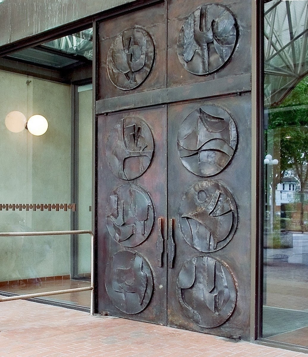 The bronze south-entrance doors of the Senate of Canada Building — two tall leaves, each carrying four circular reliefs of abstracted Canadian landscapes and wildlife, set in a glazed modernist entrance.